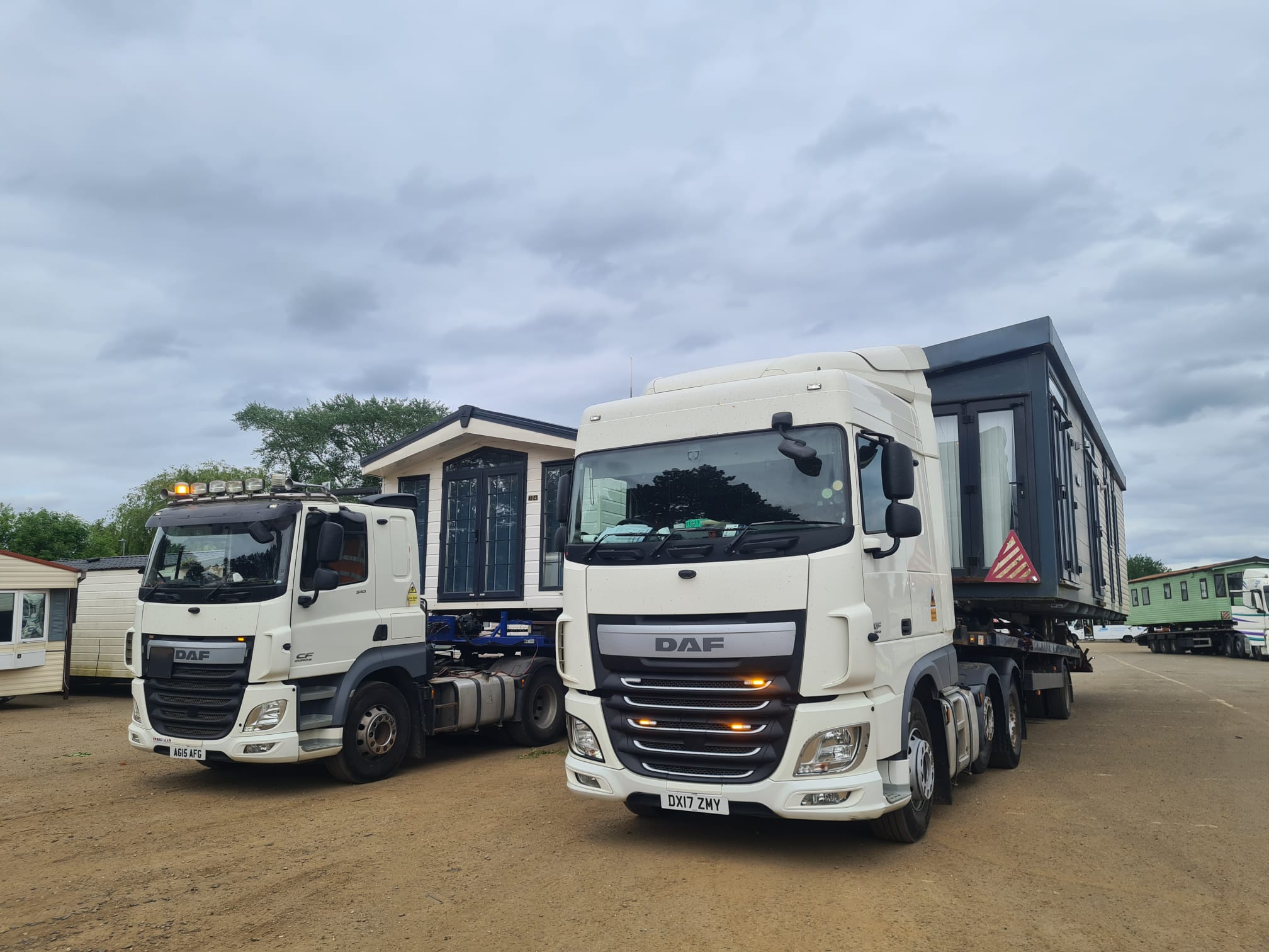 2 white flatbed lorry transporting a static caravan