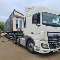 White vehicle moving a static caravan on a flatbed