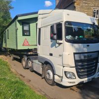 White truck carrying a static caravan on its flatbed