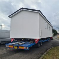 White truck delivering a large caravan unit