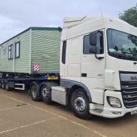 White truck loaded with a green static caravan